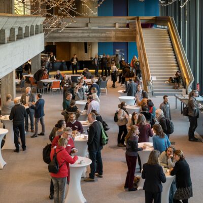 Nachhaltigkeitstagung 2018: Nachhaltigkeit first; Teilnehmende der Tagung stehen im Foyer an Stehtischen und tauschen sich aus