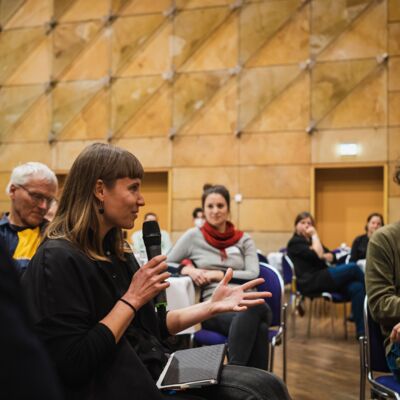 Bayerische Nachhaltigkeitstagung 2022 Nachhaltigkeit und Klimaschutz – notwendiger denn je!: Mitwirkende der Tagung sitzen im Stuhlkreis der Fishbowl-Diskussion, das Publikum ist im Hintergrund zu sehen