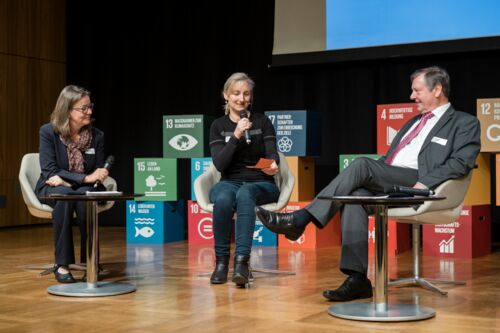 Nachhaltigkeitstagung 2018: Nachhaltigkeit first; drei Menschen sitzen auf Sesseln und tauschen sich während einer Podiumsdiskussion auf der Bühne aus