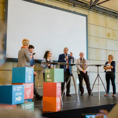 Bayerische Nachhaltigkeitstagung 2019: Handeln für den Wandel; Seitliche Aufnahme von sechs Personen, die während einer Podiumsdiskussion auf der Bühne stehen