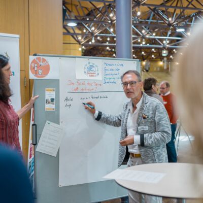 Bayerische Nachhaltigkeitstagung 2019: Zwei Referierende machen Notizen an einem Poster auf einer Pinnwand während eines Austauschs auf dem Zukunftsmarkt