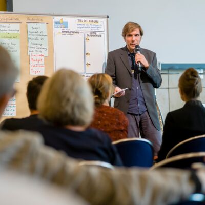 Bayerische Nachhaltigkeitstagung 2019: Handeln für den Wandel; Referent steht vor dem Publikum und gibt einen Input